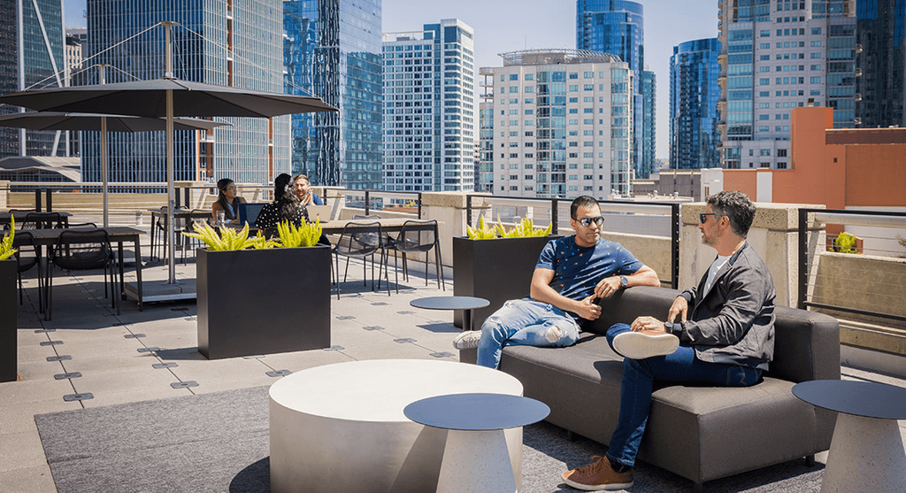 Rooftop relaxation area shown with a city backdrop and two employees are shown chatting on a couch.